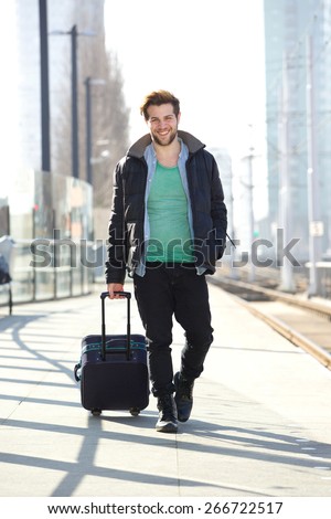 Full body portrait of a happy man walking on train station platform with bag