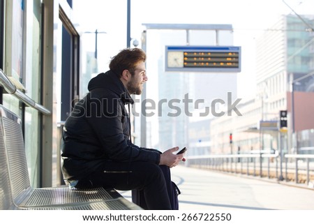 Portrait of a smiling young man sitting on bench at train station