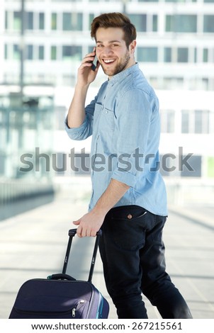 Portrait from behind of a young male traveler walking with mobile phone and bag