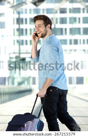 Portrait from behind of a happy young man walking at airport with bag and mobile phone