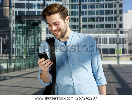 Portrait of a happy young man sending text message from mobile phone at the airport