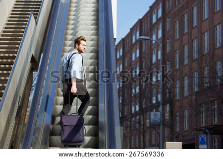 Portrait of a young man walking up escalator with travel bags
