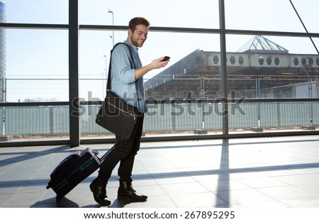 Full body portrait of a happy male traveler walking with bags and cellphone