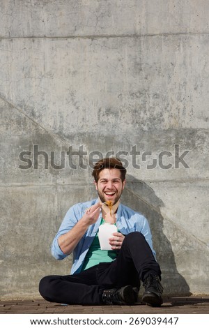 Portrait of a cheerful man eating chinese takeaway food from box with chopsticks
