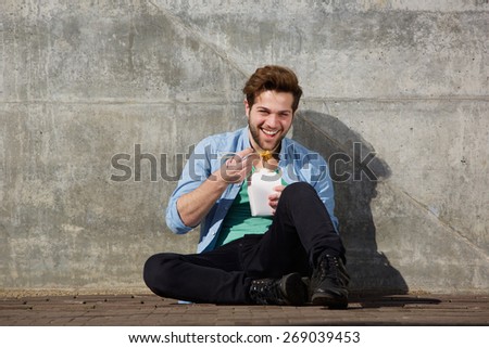 Portrait of a happy young man eating asian food with chopsticks