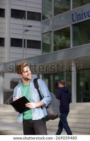 Portrait of a happy male university student standing on campus with pen and notepad