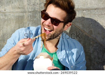 Close up portrait of a happy cool man eating chinese takeaway with chopsticks