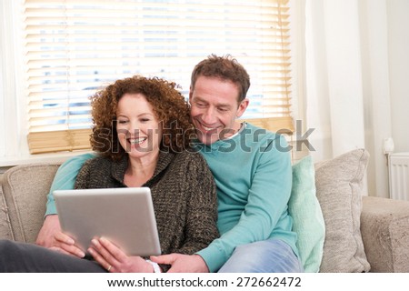 Portrait of a happy couple sitting on sofa at home looking at computer tablet