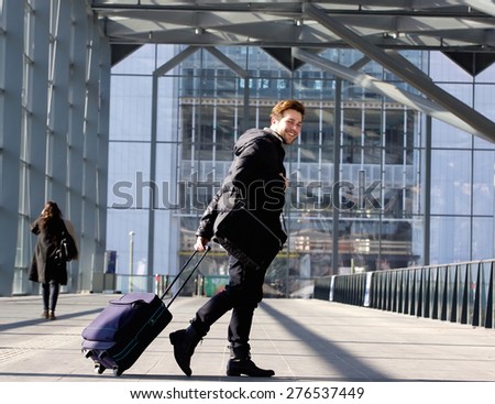 Portrait of a smiling young man walking with luggage at station