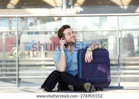 Portrait of a smiling man sitting with luggage and talking on mobile phone at airport