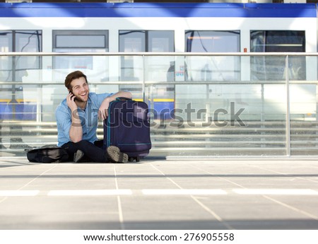 Portrait of a young man sitting on floor with bag and talking on mobile phone