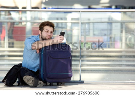 Portrait of a young man sitting on floor looking at mobile phone at airport