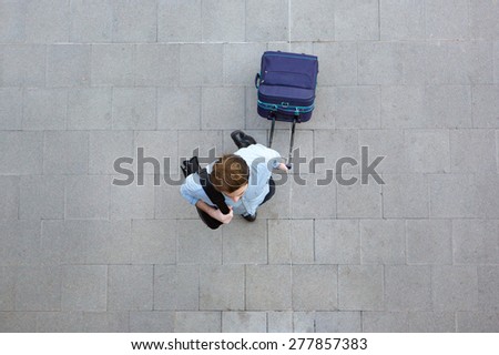 Portrait from above of a young man walking with luggage at airport