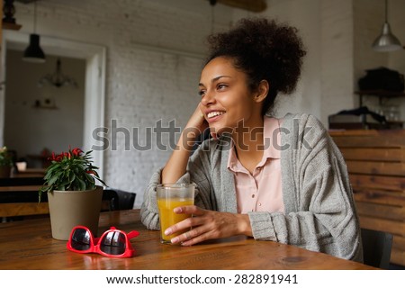 Portrait of a smiling young woman sitting at home with glass of orange juice