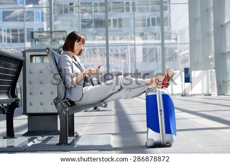 Side portrait of a business woman sitting with bag and mobile phone at airport