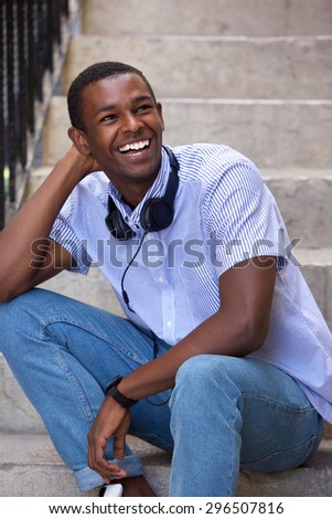 Portrait of a happy young black man sitting on steps with headphones
