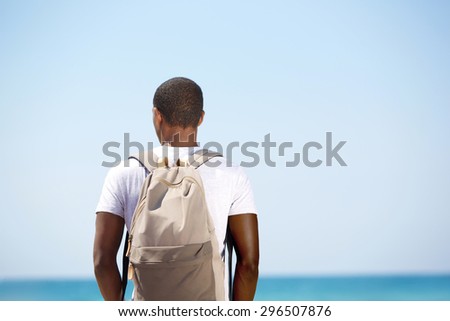 Rear portrait of a black man standing with backpack by the sea