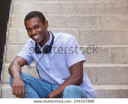 Portrait of a smiling black guy sitting on steps outside with headphones