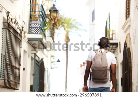 Back of young black man waking in town with bag and headphones