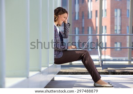 Side view of a happy business woman sitting outside using laptop
