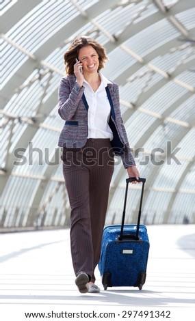 Full length business woman walking at station with bag and mobile phone