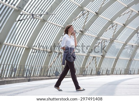 Full body side portrait of a smiling business woman walking and talking on mobile phone