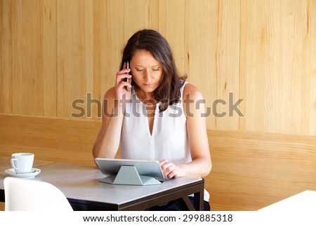 Attractive older woman in a cafe, talking on mobile phone and searching on computer tablet