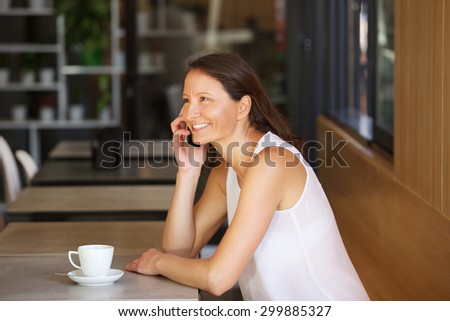 Portrait of a smiling woman in cafe talking on cell phone at a cafe