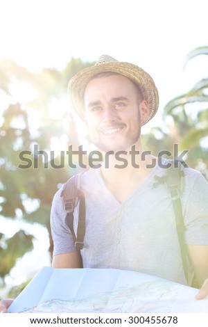 Portrait of a traveling man with bag and summer hat standing outside with a map