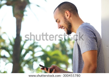 Portrait of a cheerful young man reading text message on mobile phone