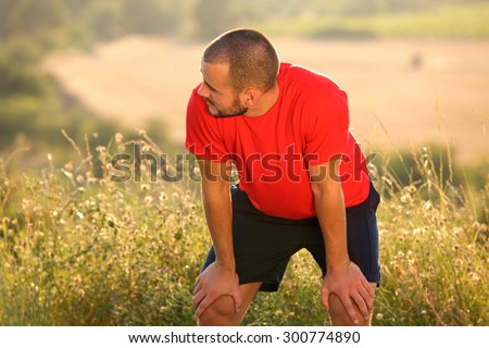 Tired young man bending down with hands on knees after workout exercise