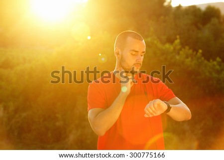 Sports man checking pulse and looking at watch during sunset