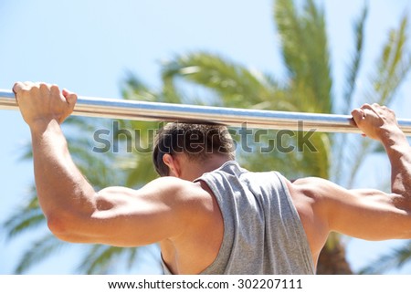Strong man exercising on pull up bar outside