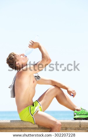 Side portrait of a fitness man drinking water from bottle after workout
