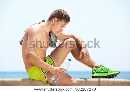 Side portrait of a tired workout man sitting by the sea with bottle of water