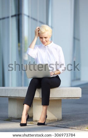 Full body cheerful young business woman using laptop outside