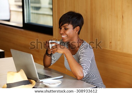 Portrait of a smiling african american woman drinking coffee and looking at laptop