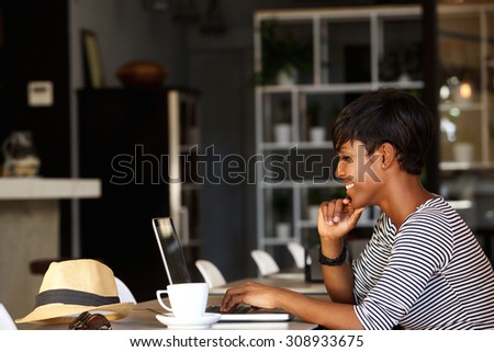 Side portrait of a smiling young african american woman using laptop in cafe