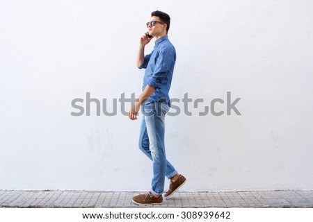Full body side portrait of a handsome young man walking and talking on cell phone