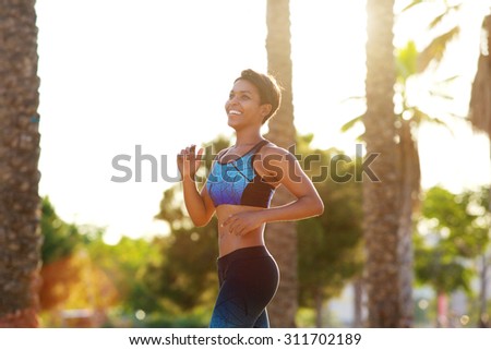 Side portrait of a smiling young african american sporty woman running in park