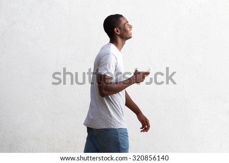 Side portrait of a cool black guy walking with cell phone against white wall