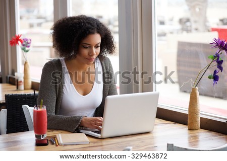 Portrait of an african american young woman sitting at cafe with laptop writing her blog