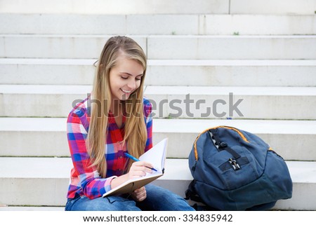 Portrait of a smiling girl sitting outside writing in book