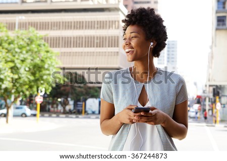 Portrait of cheerful young lady out on the city street listening to music on her mobile phone