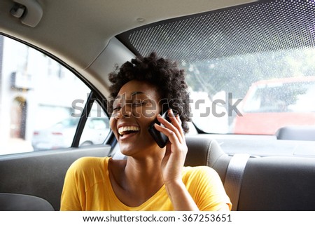 Closeup portrait of laughing young african woman sitting on a back seat of a car and talking on mobile phone