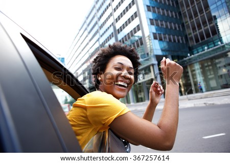 Portrait of cheerful young african woman looking out the car window with her arms raised