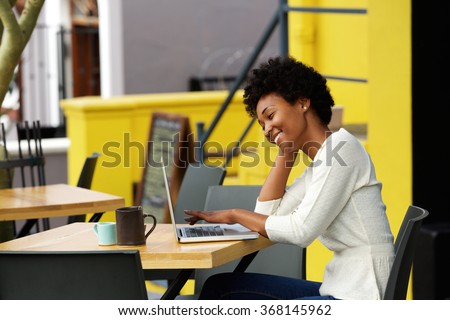 Portrait of a happy young african woman relaxing in outdoor cafe and using a laptop