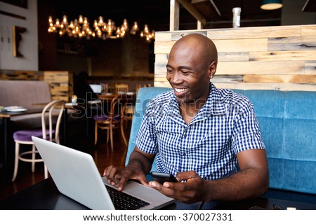 Portrait of smiling man with a mobile phone sitting at cafe using laptop