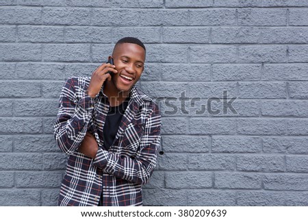 Portrait of a happy african man using mobile phone and smiling against gray wall