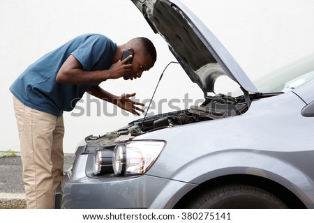 Side portrait of a young african man having trouble with his broken car calling for help on cell phone.